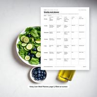 Weekly meal planner page shown filled in on a tablet screen beside a plate of salad and a bowl of blueberries